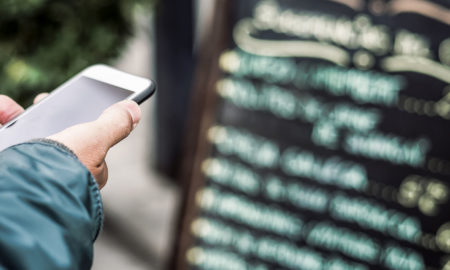 man checking restaurant reviews on Yelp or Google in front of a written menu.
