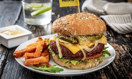 Veganer Burger von Heura mit Süßkartoffelpommes auf einem Teller angerichtet.