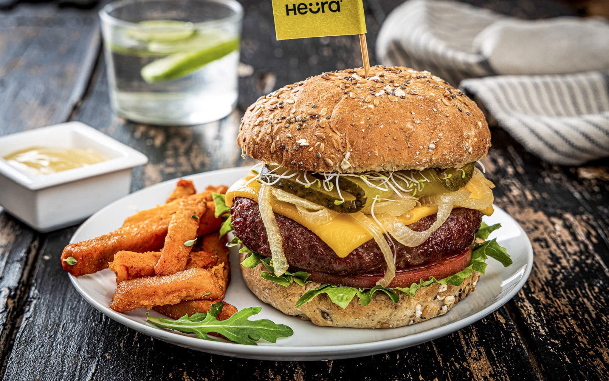 Veganer Burger von Heura mit Süßkartoffelpommes auf einem Teller angerichtet.