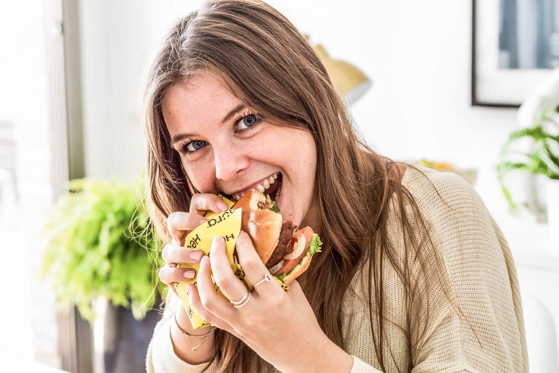 Young woman bites with relish into a plant burger from Heura.