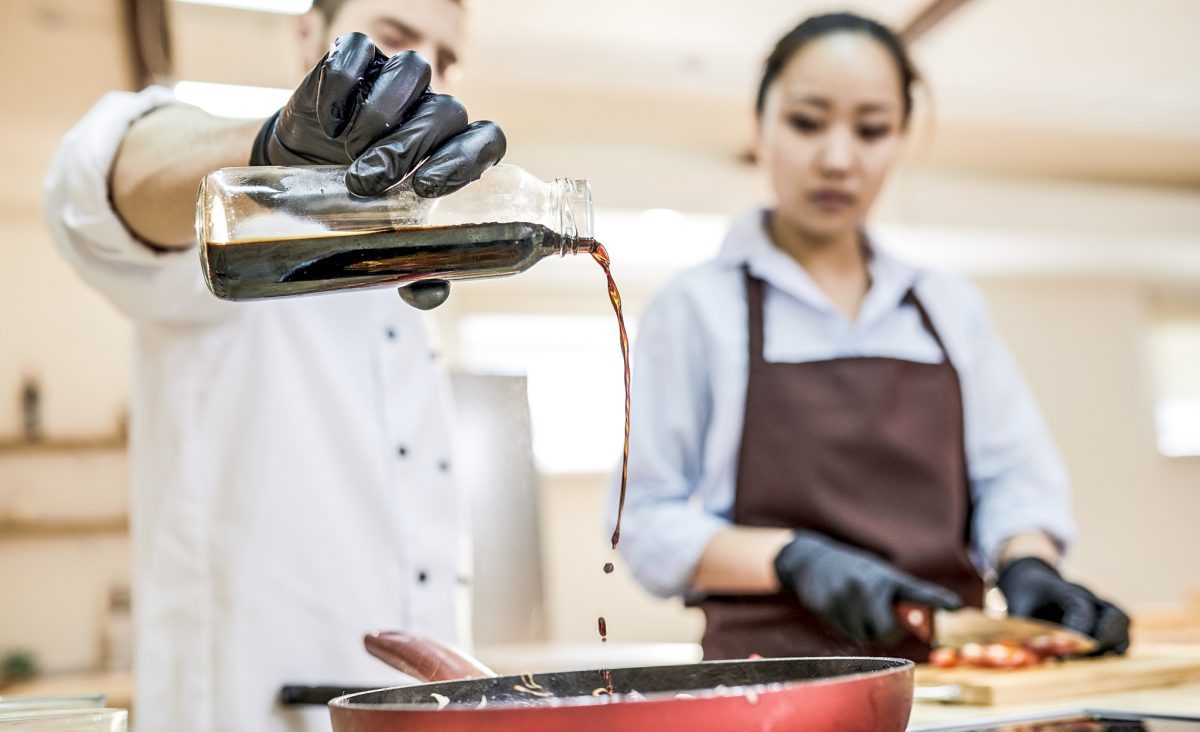 El cocinero refina un plato con salsa de soja bajo la estricta mirada del chef.