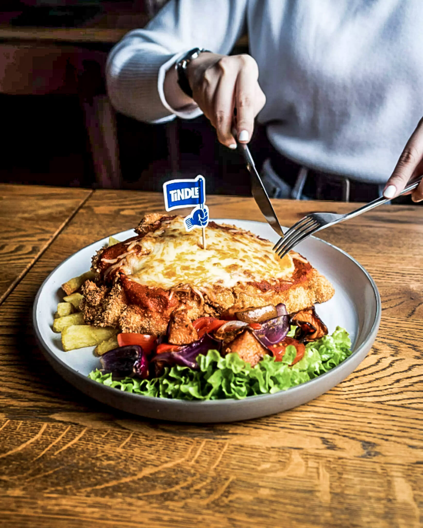 TiNDLE's plant-based chicken schnitzel, topped with melted vegan cheese and served with a side of crispy fries, fresh greens, and roasted vegetables.