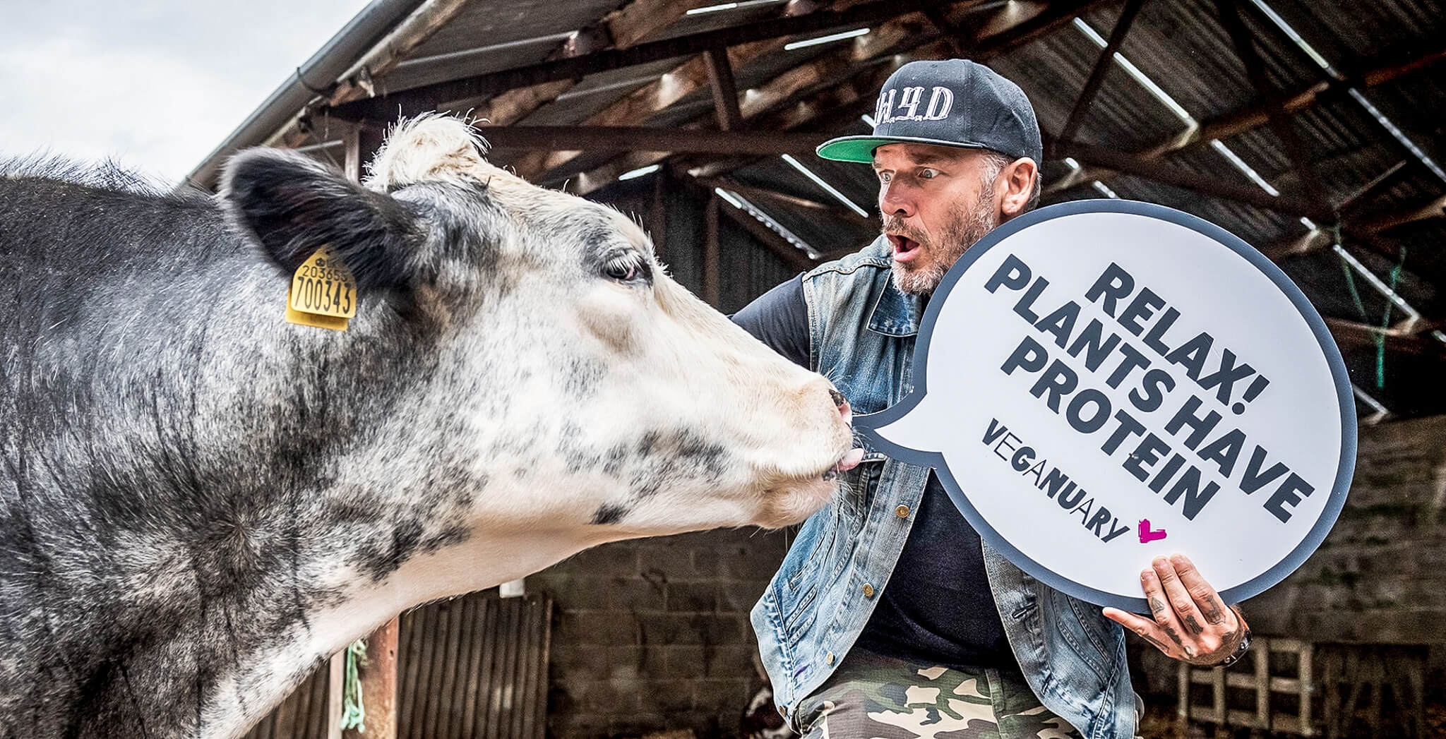 Hombre acariciando a una vaca y sosteniendo un cartel que dice "Tranquilos, las plantas tienen proteínas".