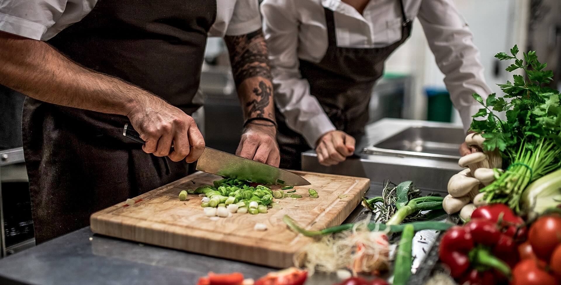 Koch trainiert mit Mitarbeiter das richtige schneiden von Gemüse in der Restaurantküche