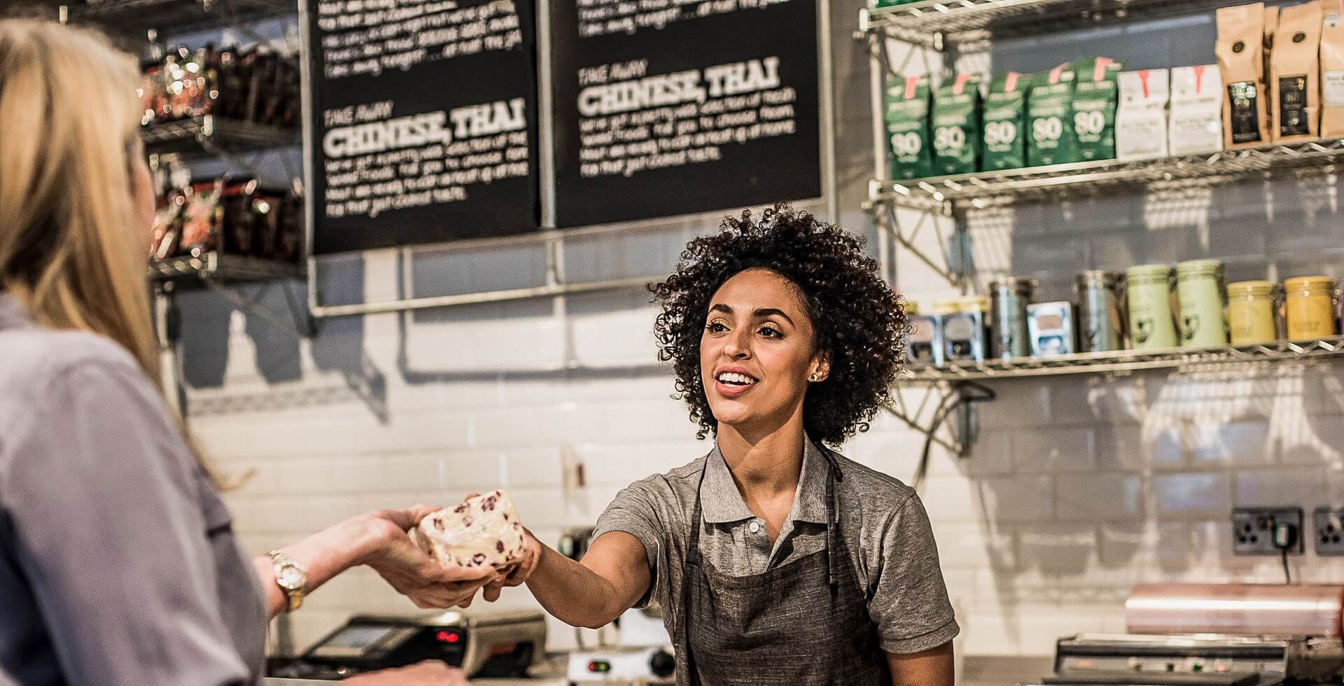Saleswoman handing a customer a hot meal over the counter in a supermarket.